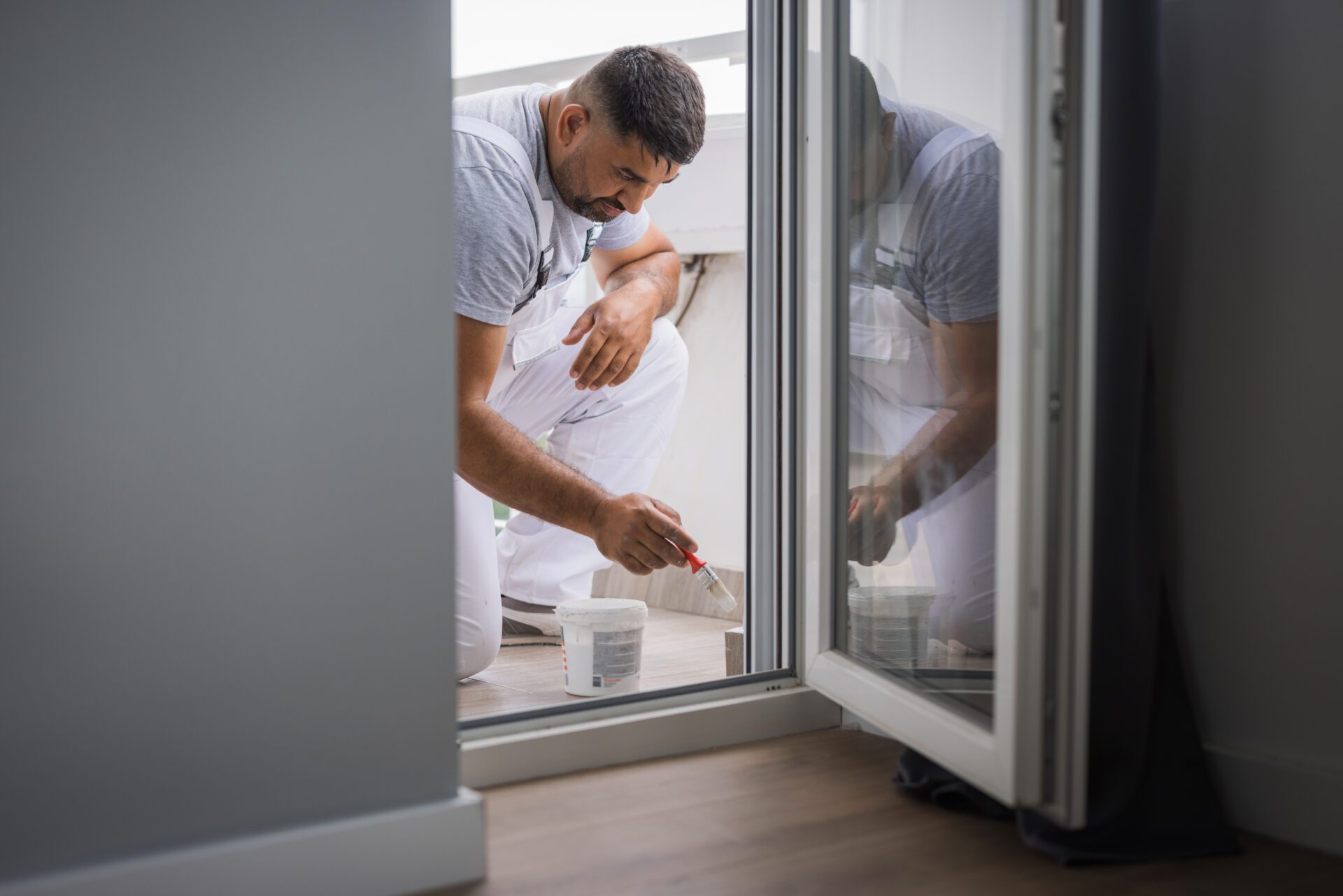 Man painting outside through glass door.