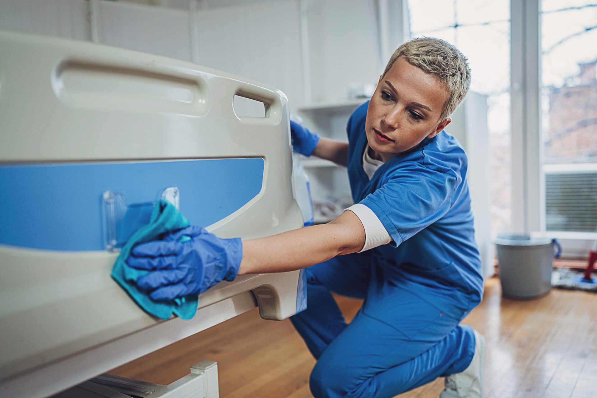 Nurse cleaning hospital bed with cloth.